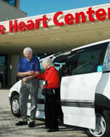 Volunteer helping elderly client out of van at medical center